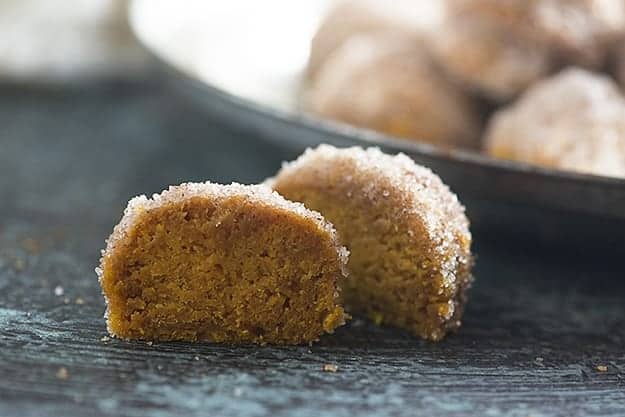 A donut hole cut in half on a wooden table in front of a tray of donut holes.