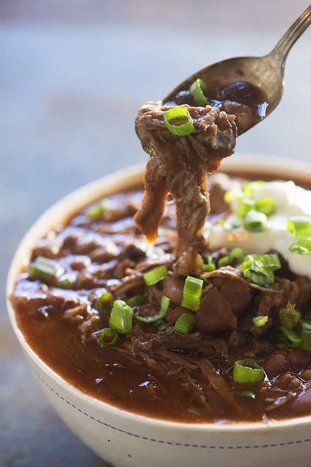 A spoon scooping out a bite of chili from a bowl.