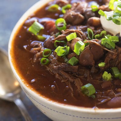 A close up of a cup of chili topped with chives.