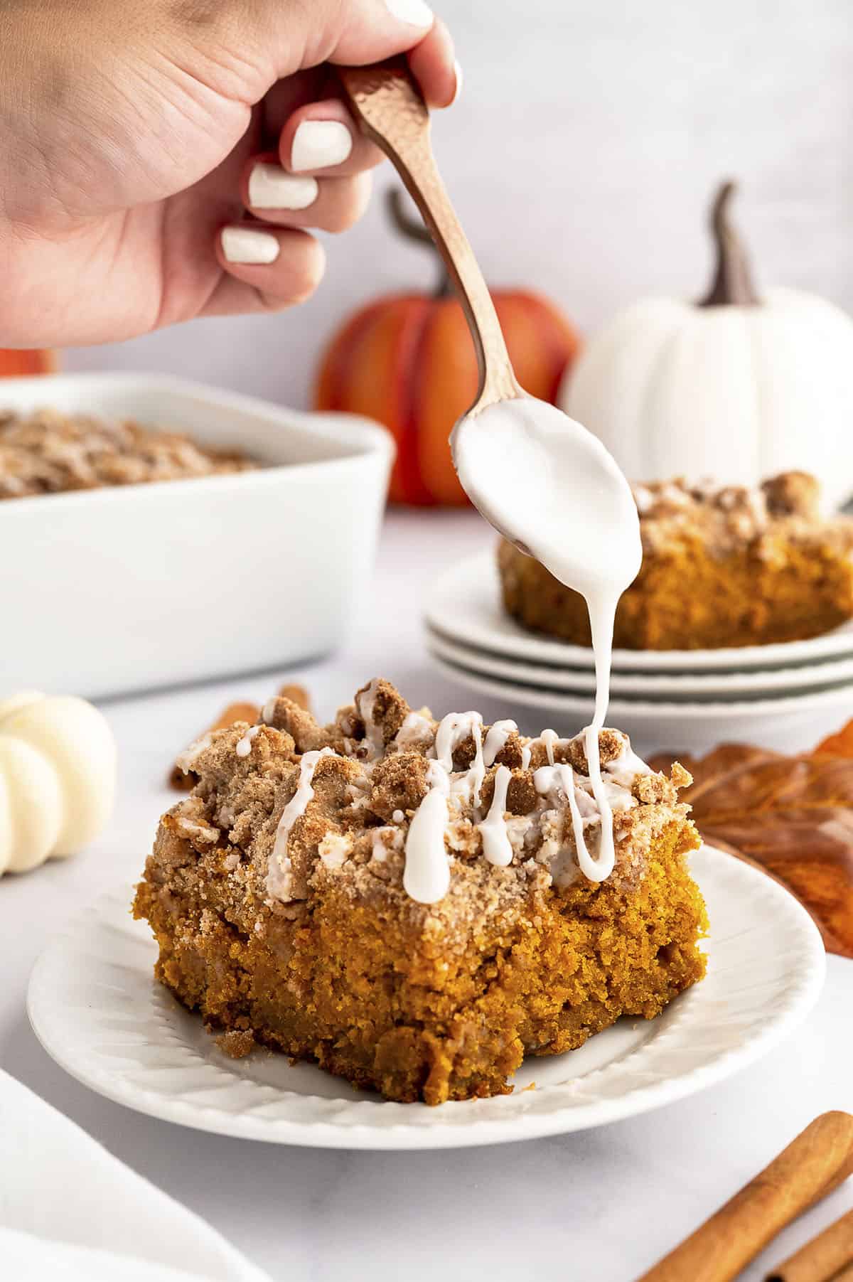 Person drizzling vanilla glaze over pumpkin coffee cake.