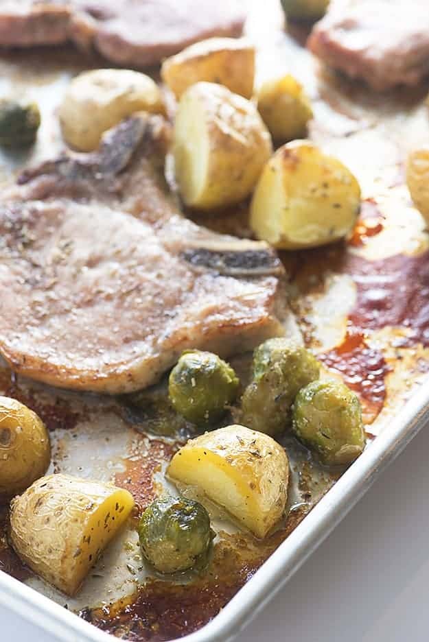 Pork chops, Brussel sprouts, and potatoes on a baking sheet.