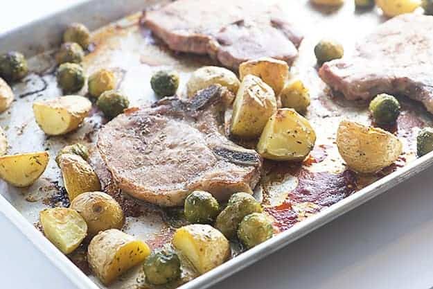A baking sheet with bone-in pork chops, potatoes, and Brussel sprouts.
