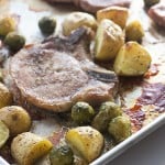 Pork chops, potatoes, and Brussel sprouts on a baking sheet.