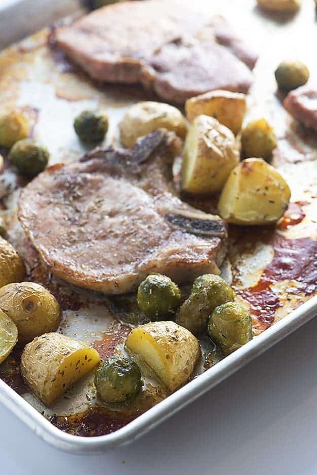 Pork chops, potatoes, and Brussel sprouts on a baking sheet.