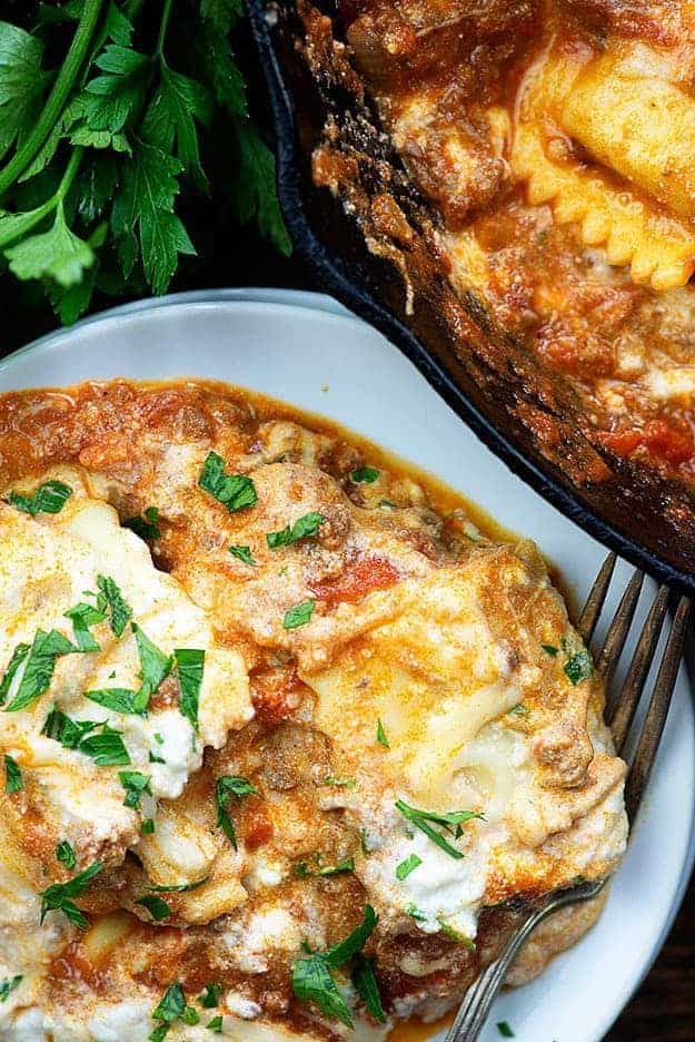 A close up of a plate of lasagna next to a cast-iron skillet.