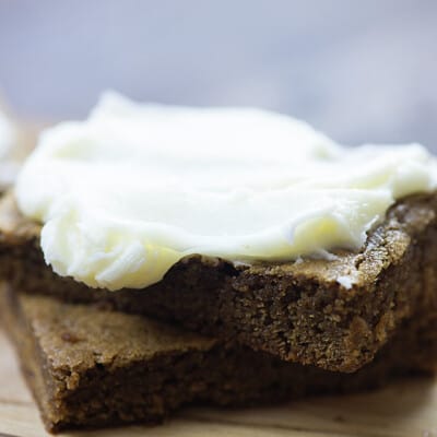 Two gingerbread squares topped with frosting on a cutting board.