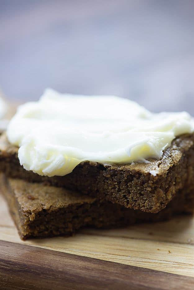 Two gingerbread squares topped with frosting on a cutting board.