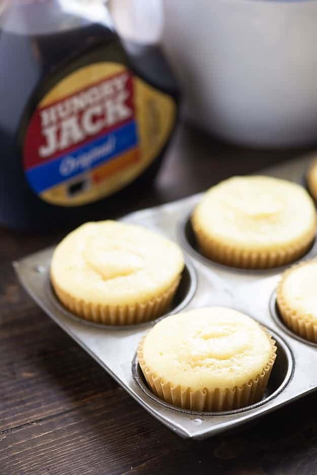Pancake muffins in a muffin pan in front of a bottle of syrup.