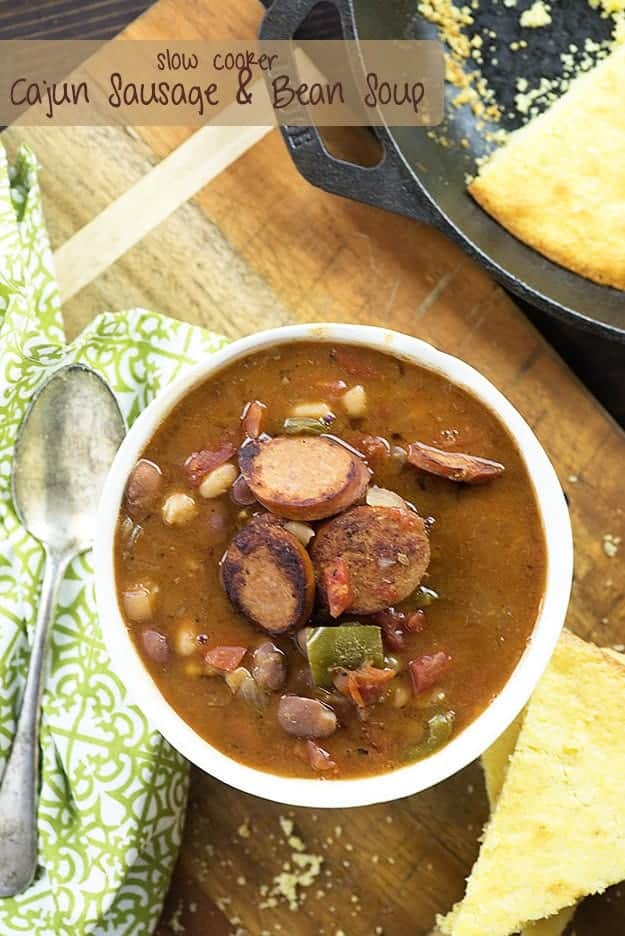 A white cup of sausage and bean soup on a cloth napkin.