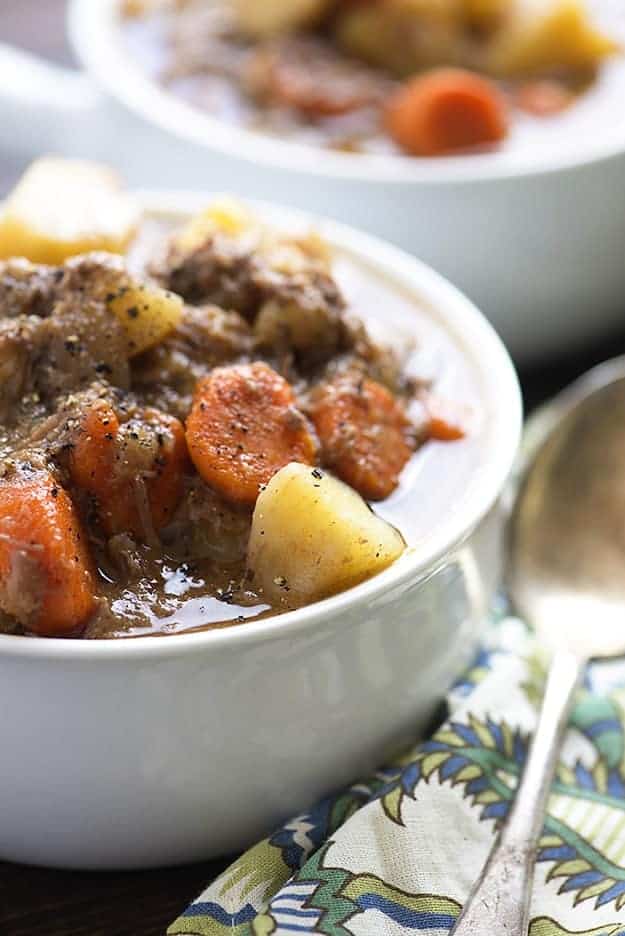 A cup of beef stew next to a silver spoon.