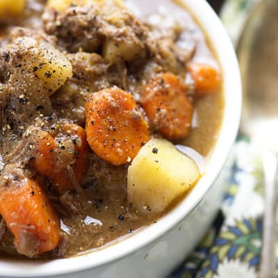 A cup of beef stew with carrots and potatoes.