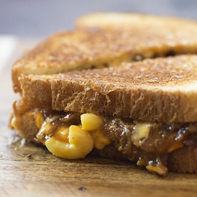 A close up of a macaroni and cheese sandwich cut in half on a cutting board.