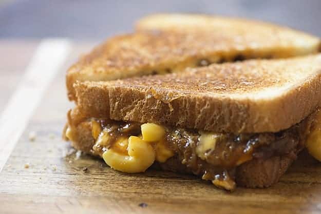 A close up of a macaroni and cheese sandwich cut in half on a cutting board.