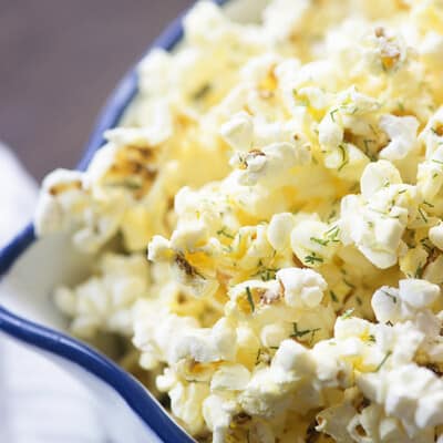 Popcorn topped with dill in a  white bowl.