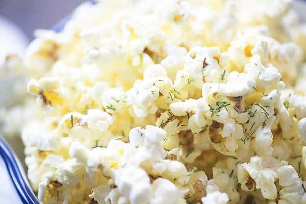 A close up of a bowl of popcorn topped with dill and parmesan.