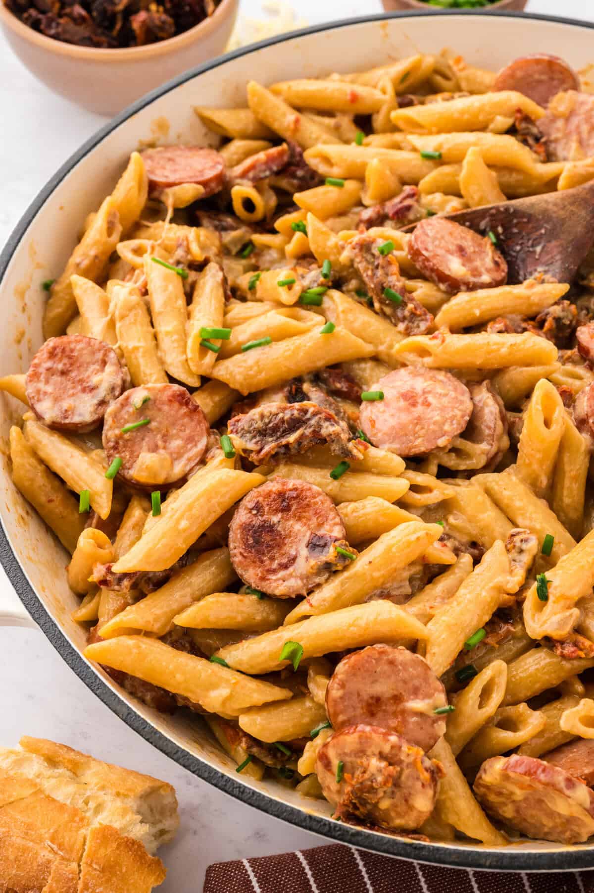 Smoked sausage, penne, and sun-dried tomatoes in white skillet.