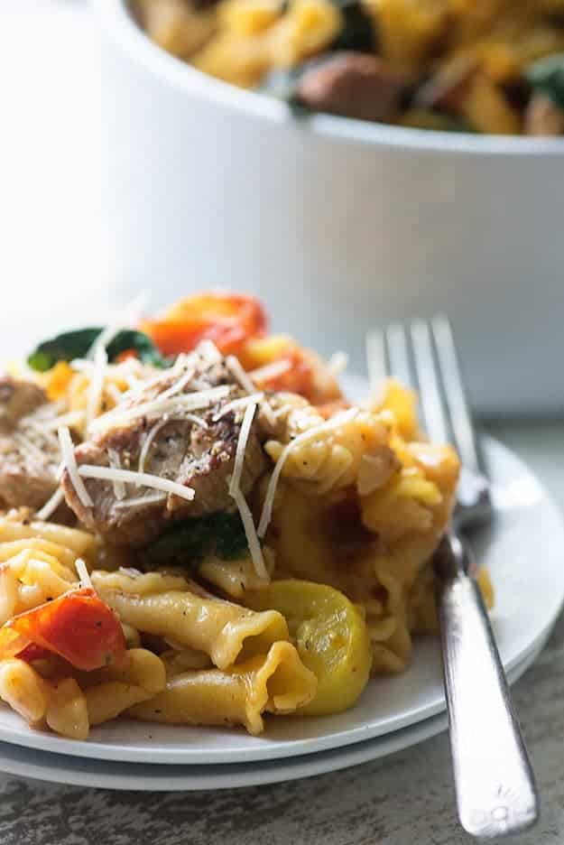 Pasta topped with pork chunks and cheese on a white plate.