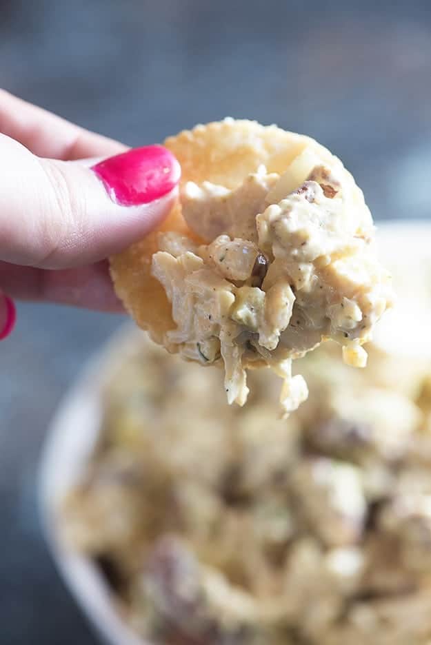 A close up of a woman holding a cracker dipped into chicken salad.