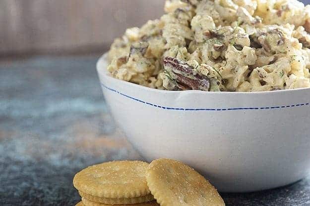 A bowl of loaded chicken salad next to a small stack of Ritz crackers.