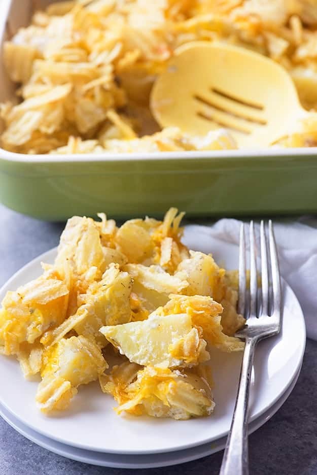 A close up of a plate of cheddar potatoes in front of a pan of potatoes.