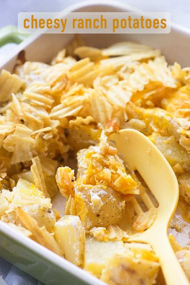 A close up of a large plastic spoon scooping up a potato casserole.