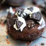 A close up of a piece of chocolate donut topped with oreo pieces.