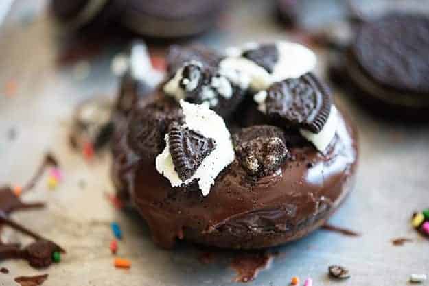 A close up of a piece of chocolate donut topped with oreo pieces.