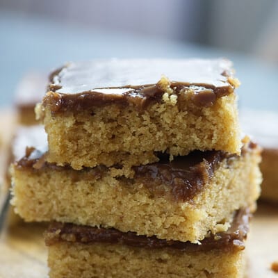 A few squares of peanut butter cake topped with chocolate frosting stacked on top of each other.