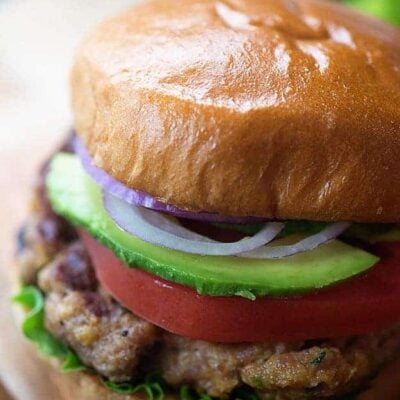 A close up of a turkey burger with avocado, onion, and tomatoes.