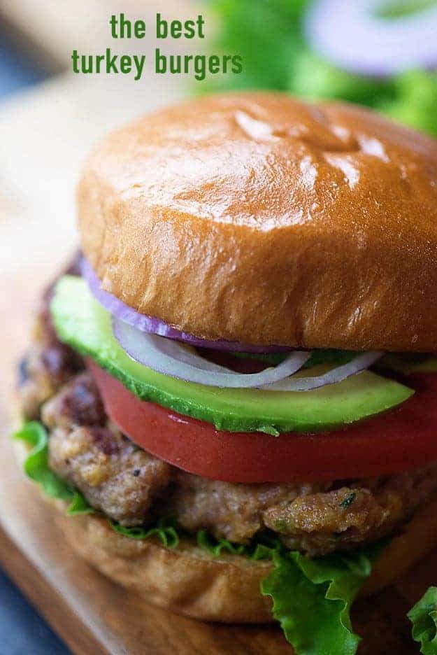 A close up of a turkey burger with avocado, onion, and tomatoes.