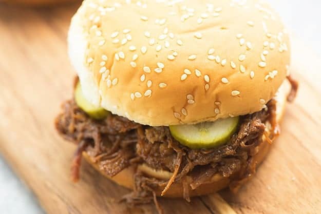 A close up of a pulled beef sandwich sitting on top of a wooden table