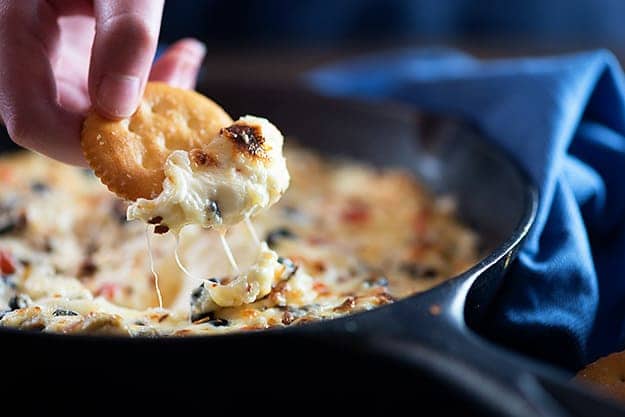 A person dipping a Ritz cracker into a dip that is in a black cast-iron skillet.