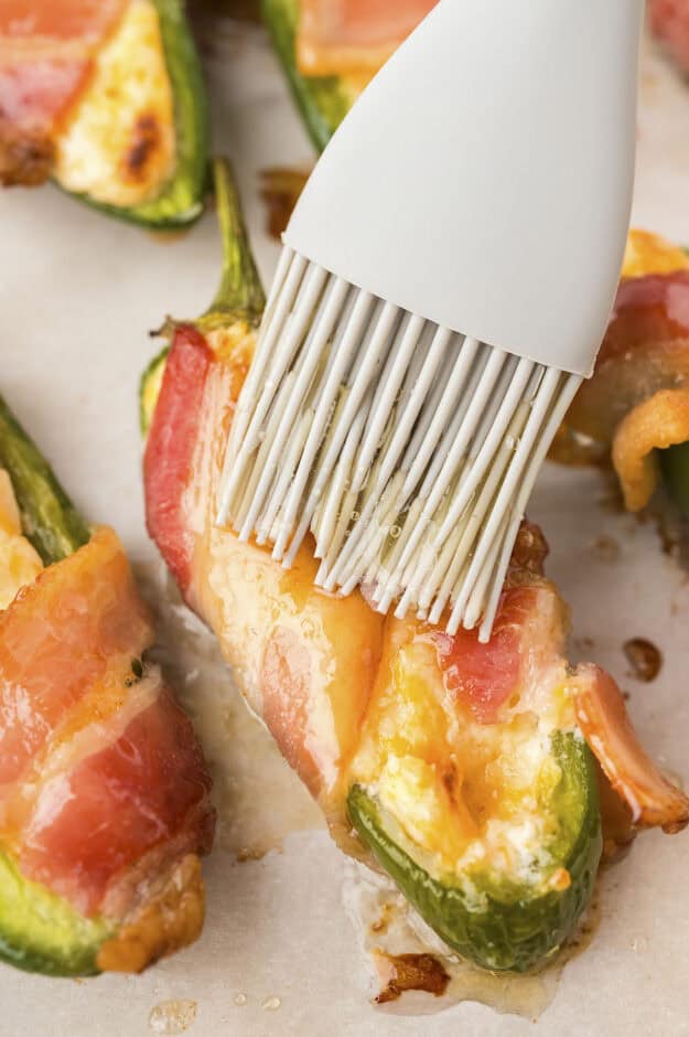 Honey being brushed on a bacon wrapped jalapeno popper.
