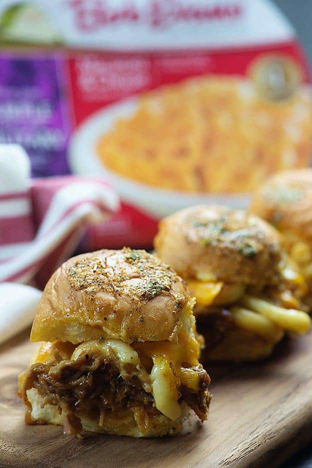 Several sliders lined up in front of a box of macaroni and cheese.