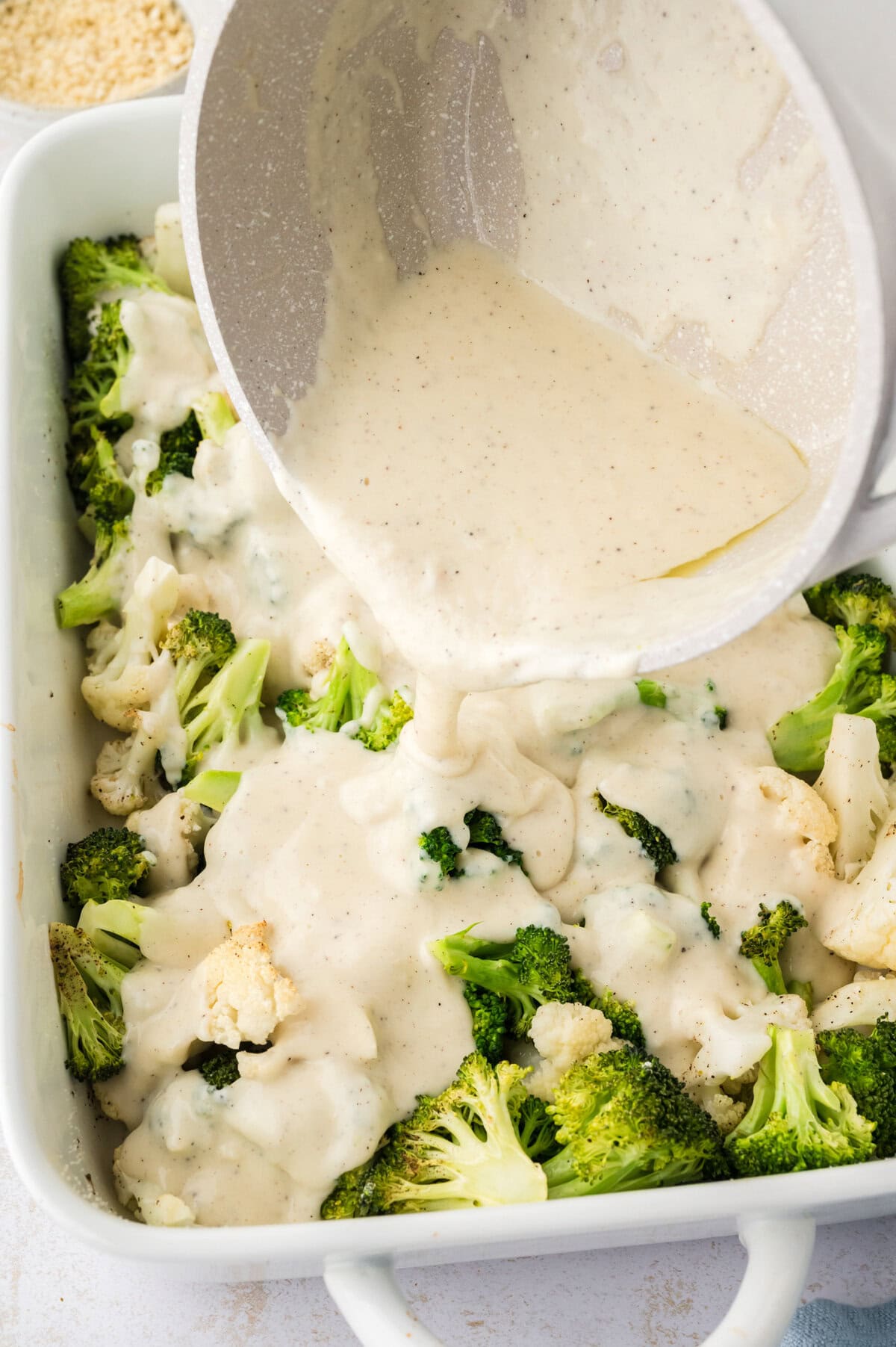 Cheese sauce being poured over roasted vegetables.