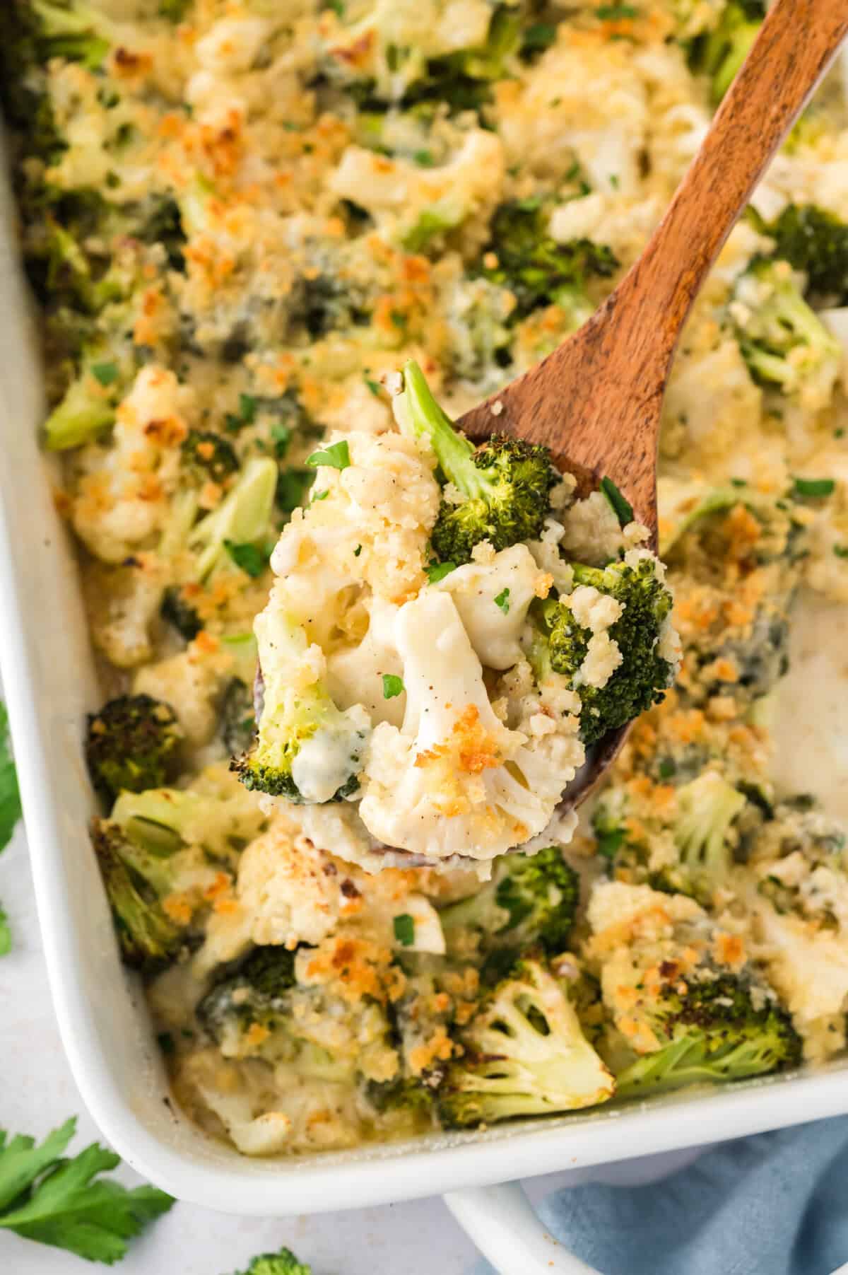 Broccoli and cauliflower au gratin on wooden spoon over baking dish.