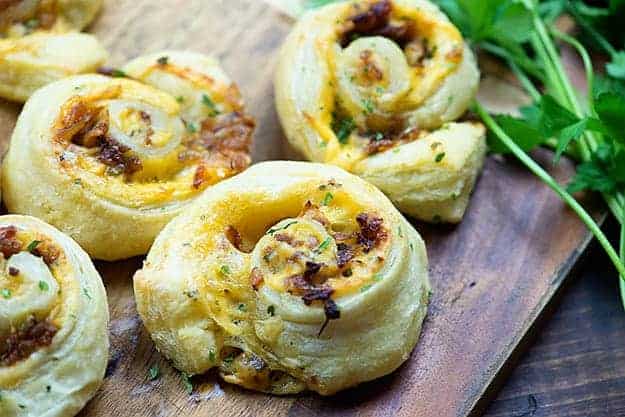 Cutting board with a cheesy pinwheel topped with carmelized onions.