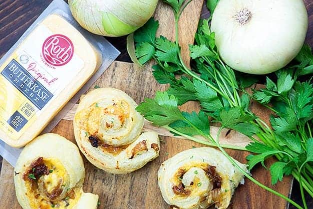 Onions and garnishments on a cutting board with pinwheel pastries.