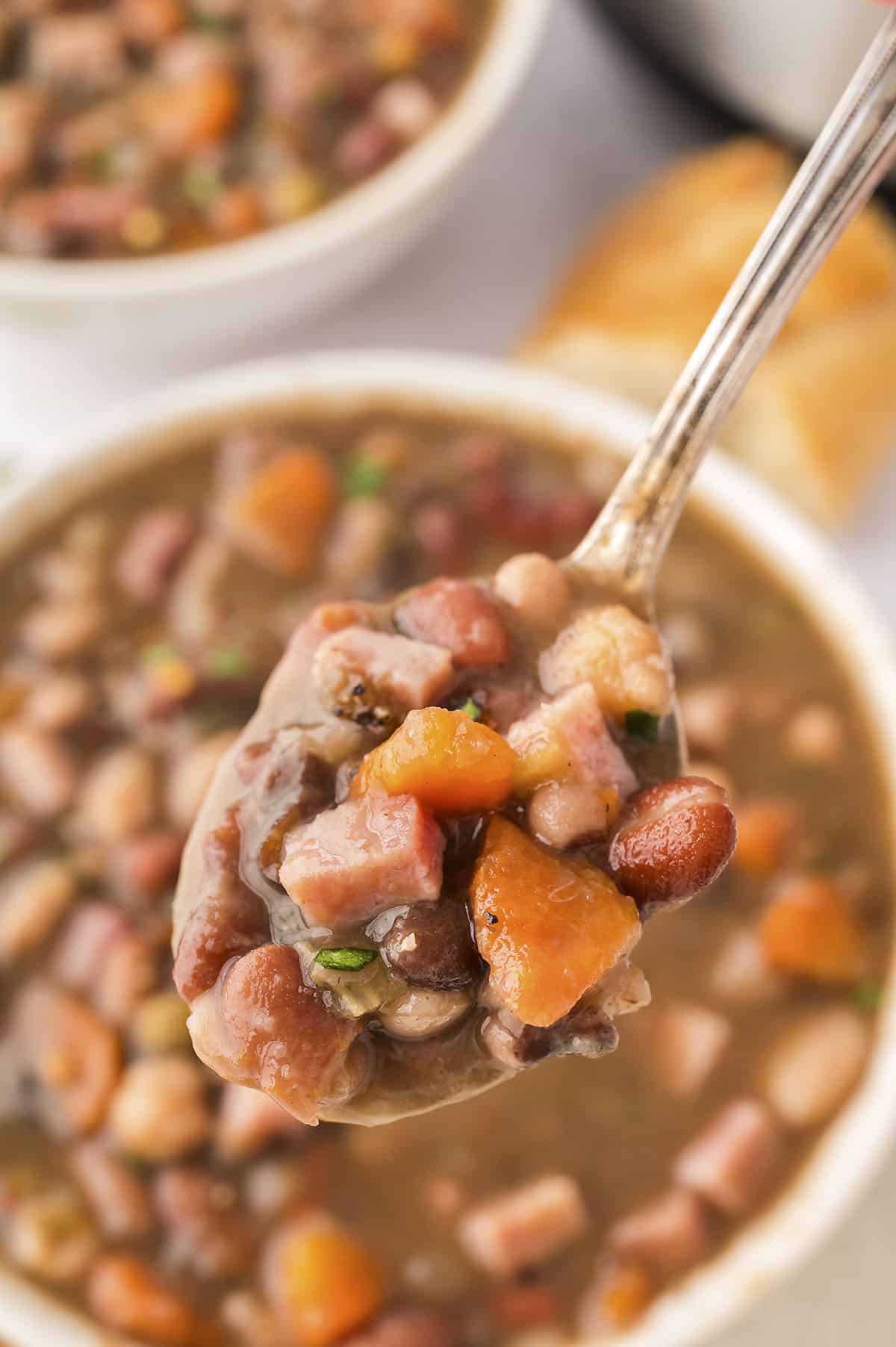 Instant Pot ham and bean soup on spoon over white bowl.