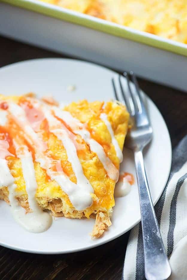 A square piece of casserole with ranch drizzled over the top on a white plate.