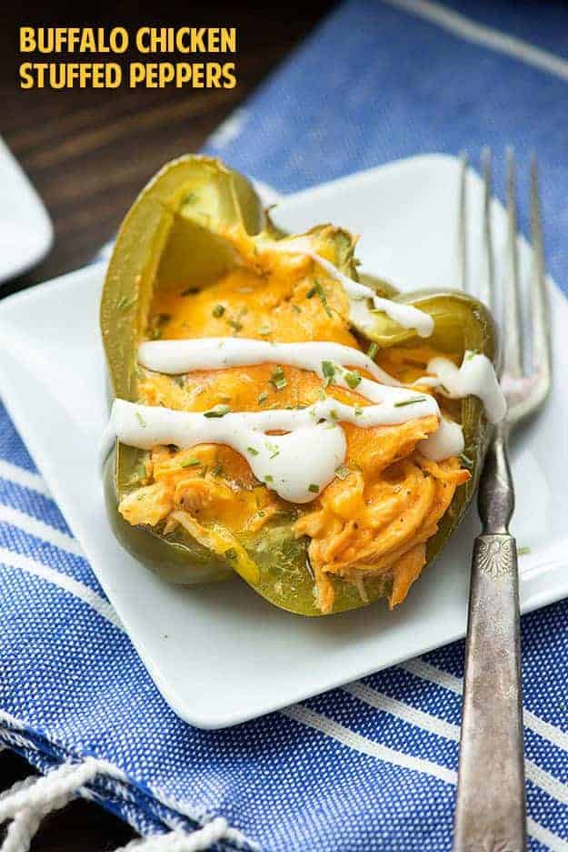 A stuffed red pepper on a square white plate with a fork.