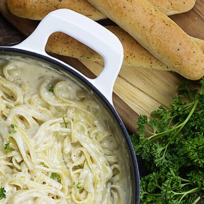A pot of alfredo noodles next to a stack of breadsticks.