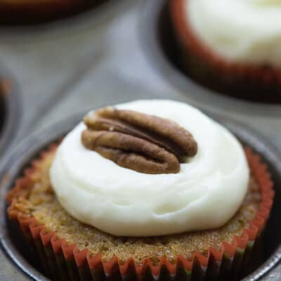 A close up of a cupcake with white icing and a pecan on top.