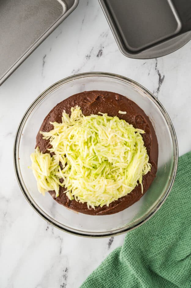 Shredded zucchini being added to bread batter.