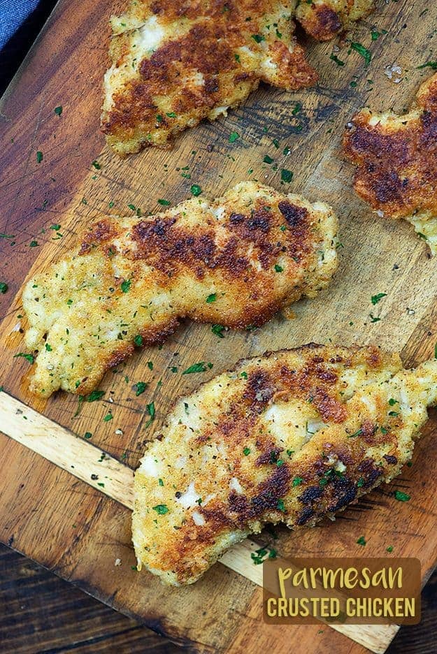 Several parmesan chicken breasts on a cutting board.