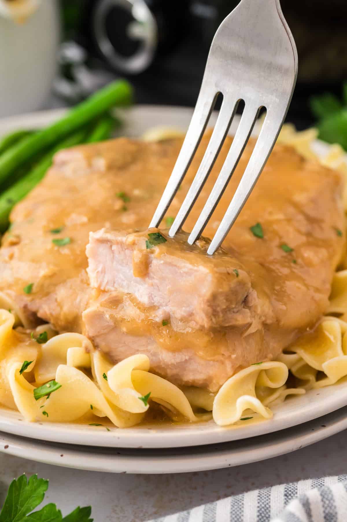 Fork taking a piece of smothered pork chop off plate.