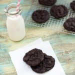 Two chocolate cookies on a napkin in front of a jar of milk