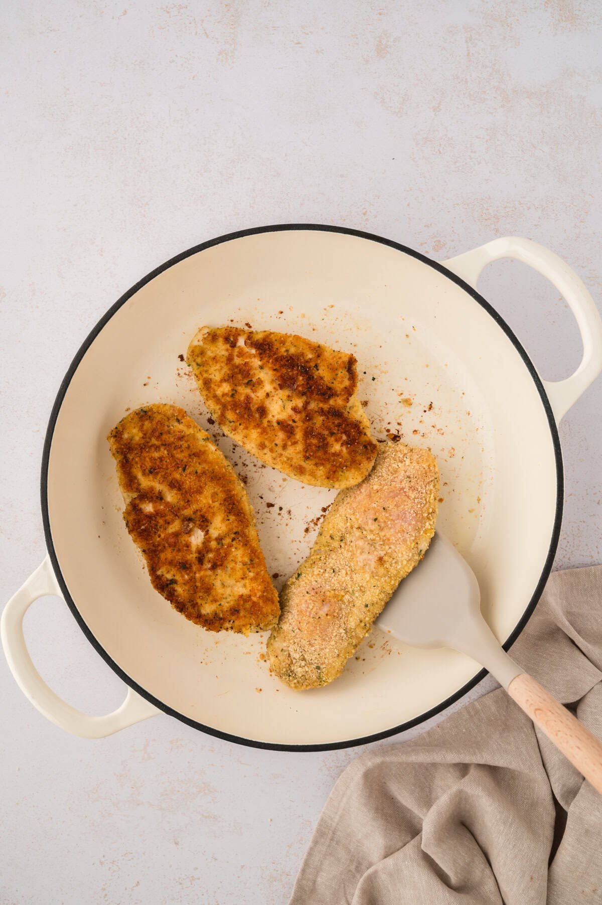 Parmesan crusted chicken cooking in a skillet.