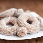 A close up of a few sugar coated donuts on a plate.