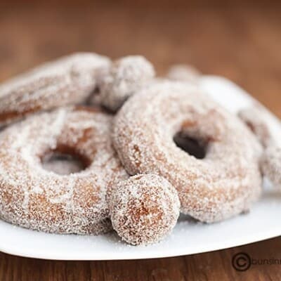 A close up of a few sugar coated donuts on a plate.